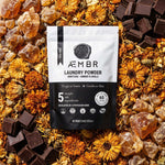 AEMBR non-toxic laundry powder pouch on dried flowers, chocolate chunks, and amber crystals