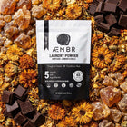 Non-toxic laundry detergent powder packaging with amber, flowers, and chocolate pieces.