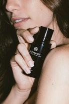 Woman holding AEMBR Alkymist fragrance bottle close to face, promoting non-toxic home scent.