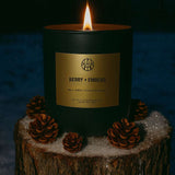 Candle labeled 'Berry & Embers' on a wooden stump with pine cones against a dark background