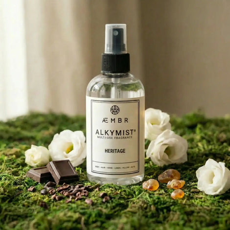 Non-toxic multi-use fragrance spray with chocolate, white flowers, and amber stones on moss.