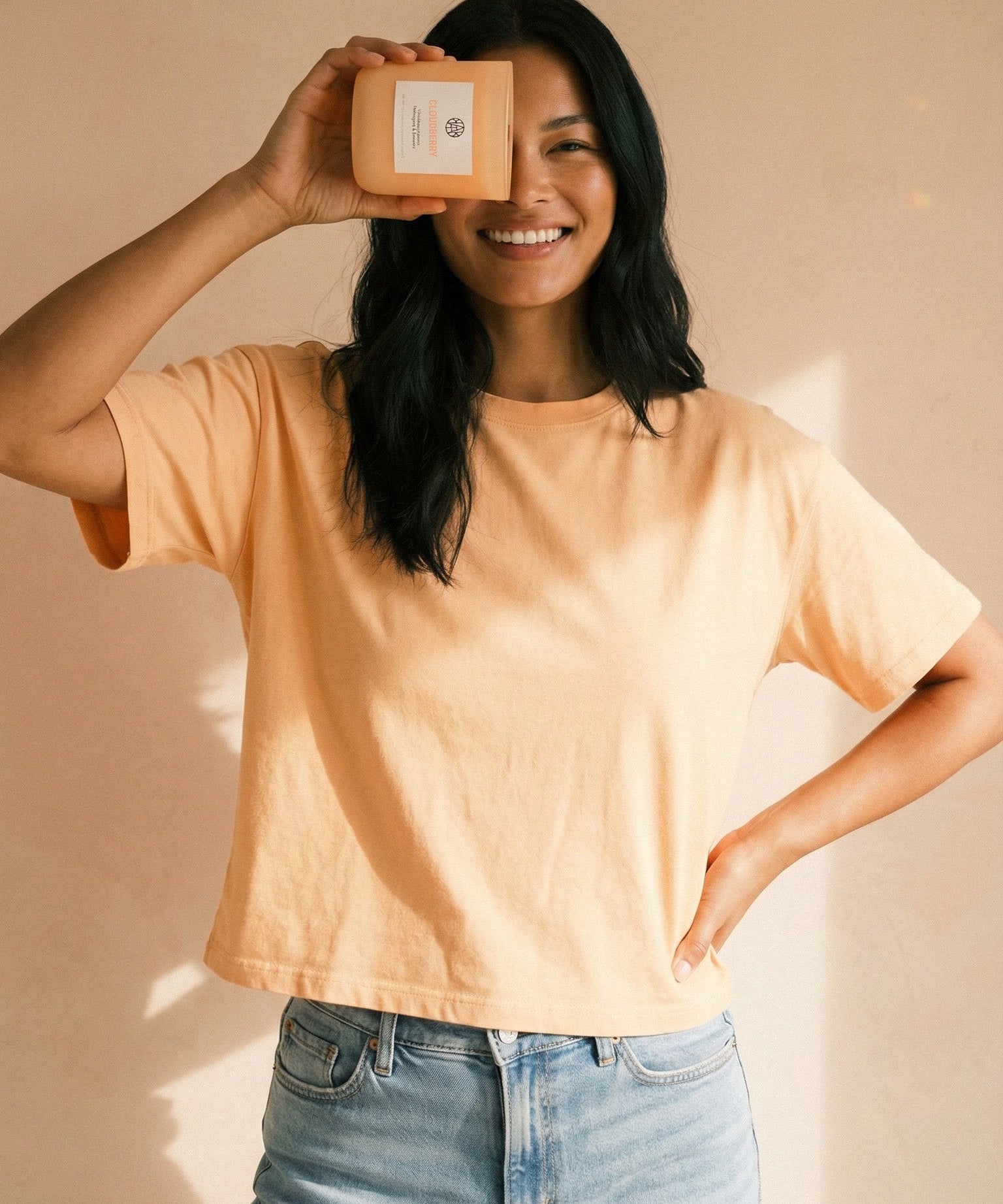 Person wearing a light yellow shirt and blue jeans holding a small box against a beige background