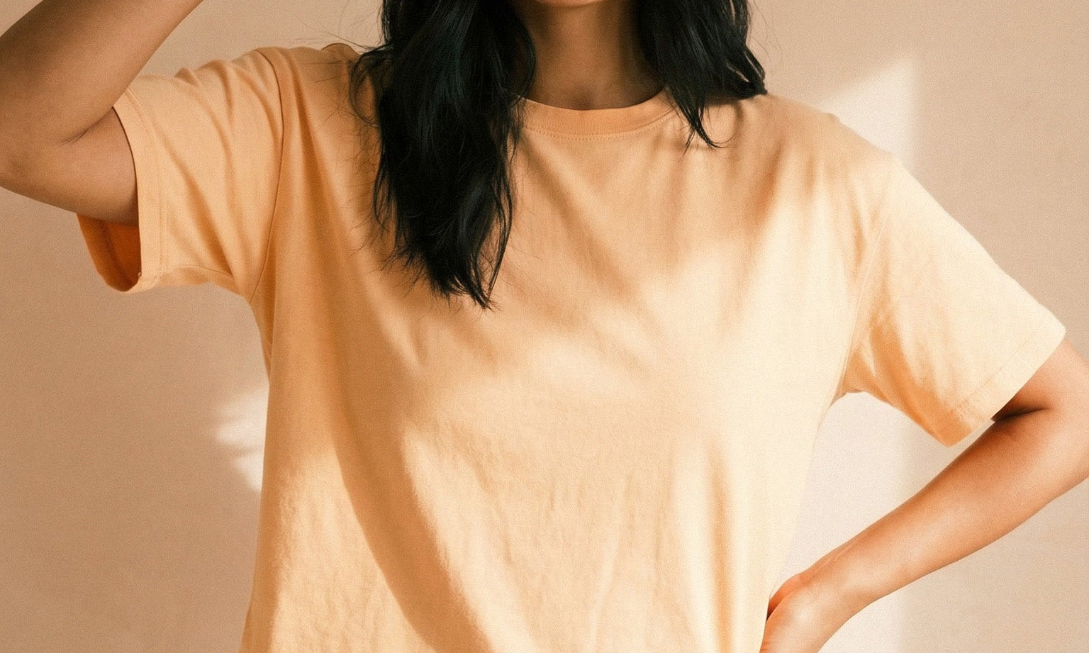 Person wearing a light yellow shirt and blue jeans holding a small box against a beige background