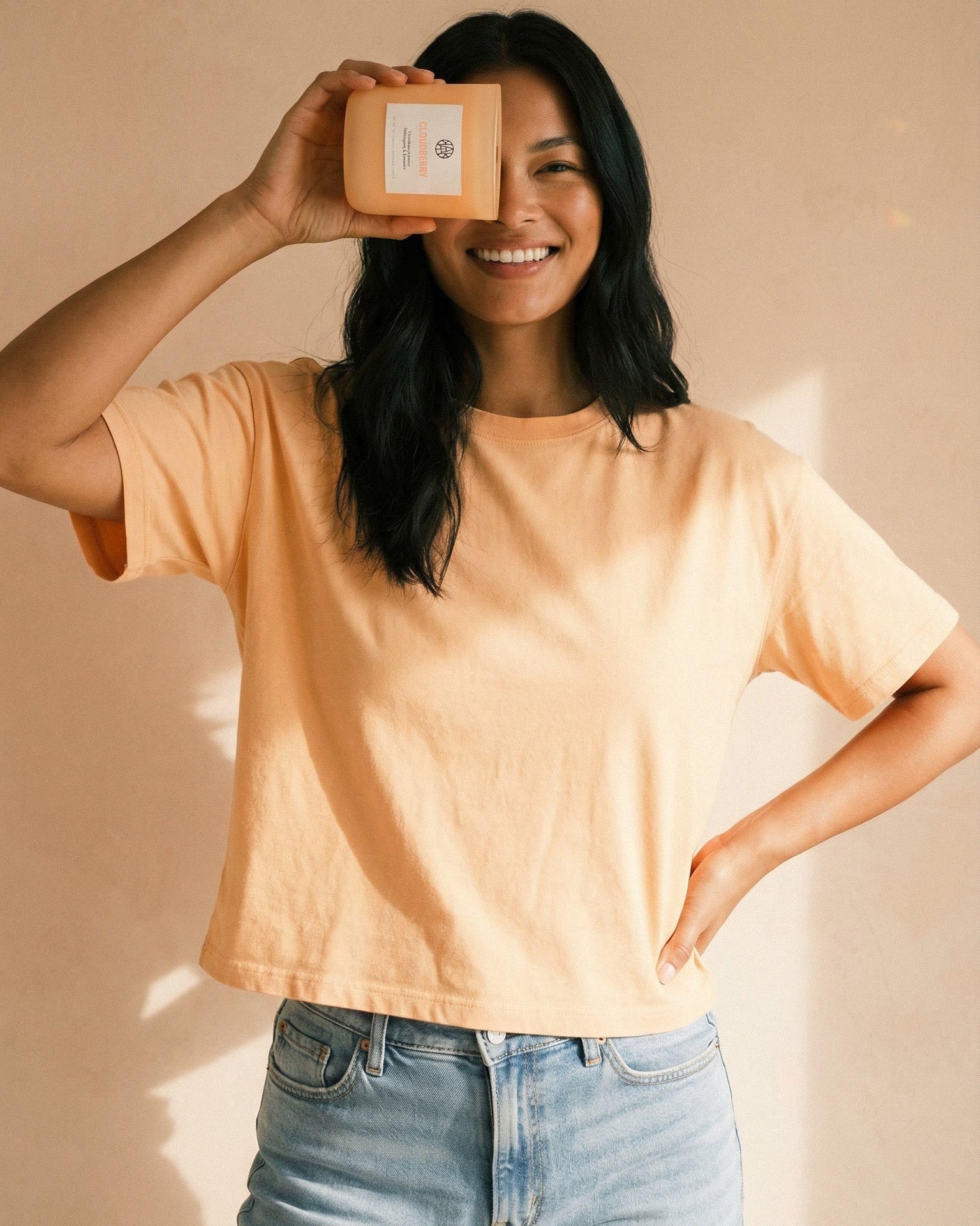 Person wearing a light yellow shirt and blue jeans holding a small box against a beige background