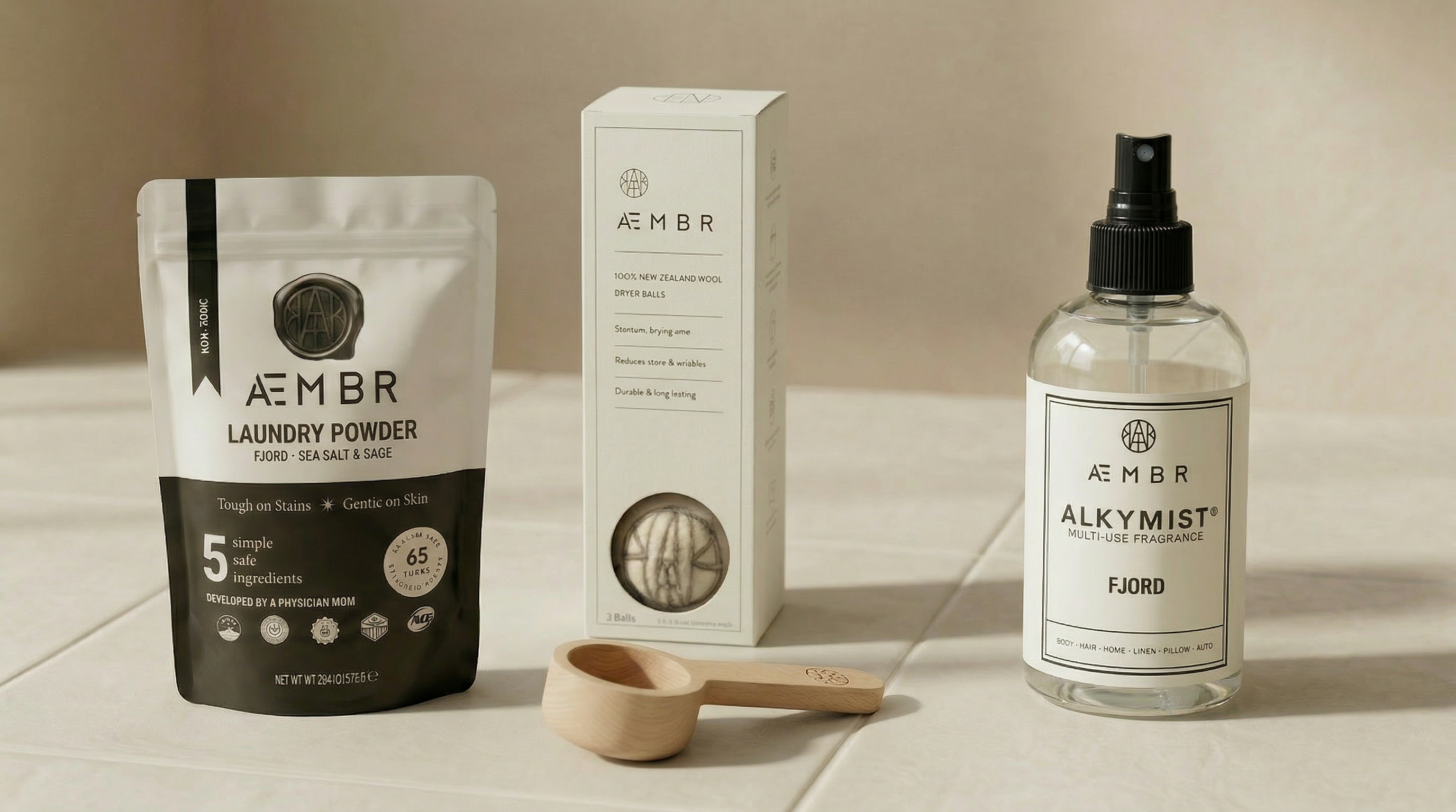Aembr laundry powder package, box, and Alkymist bottle on a neutral background