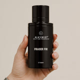 Black Alkymist Fraser Fir perfume bottle held in a hand against a beige background 