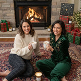 Two women sitting by a fireplace with Christmas decorations and presents.