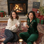 Two women sitting by a fireplace with Christmas decorations and presents.