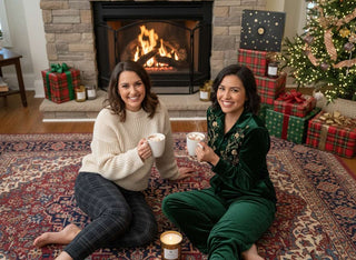 Two women sitting by a fireplace with Christmas decorations and presents.