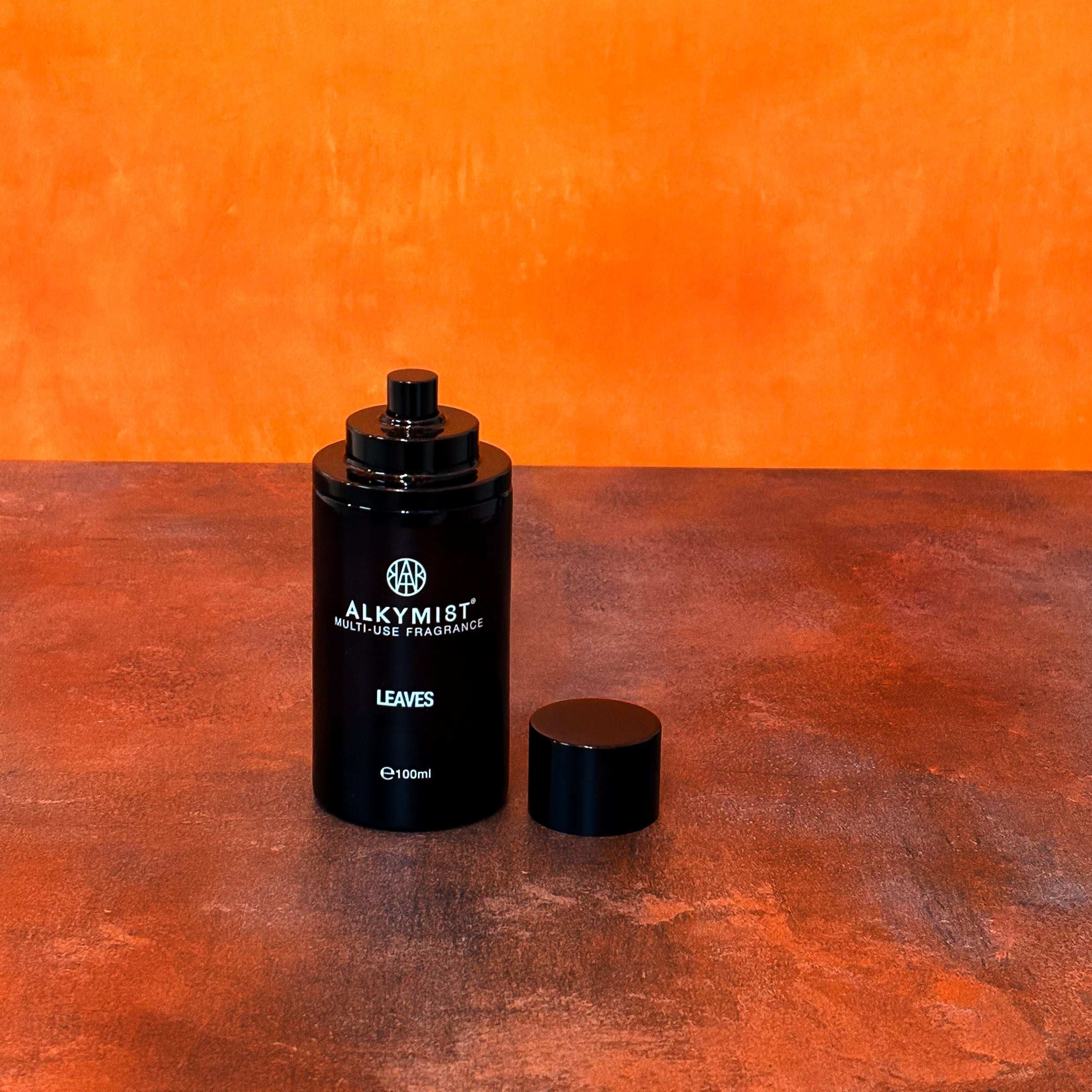 AEMBR non-toxic ALKYMI8T multi-use fragrance bottle labeled 'LEAVES' on a warm orange surface