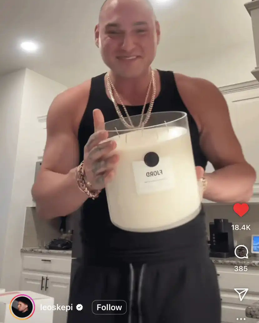 Smiling man in kitchen holding large AEMBR FLORD non-toxic candle