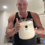 Smiling person holding a large AEMBR FLORO non-toxic candle in a modern kitchen