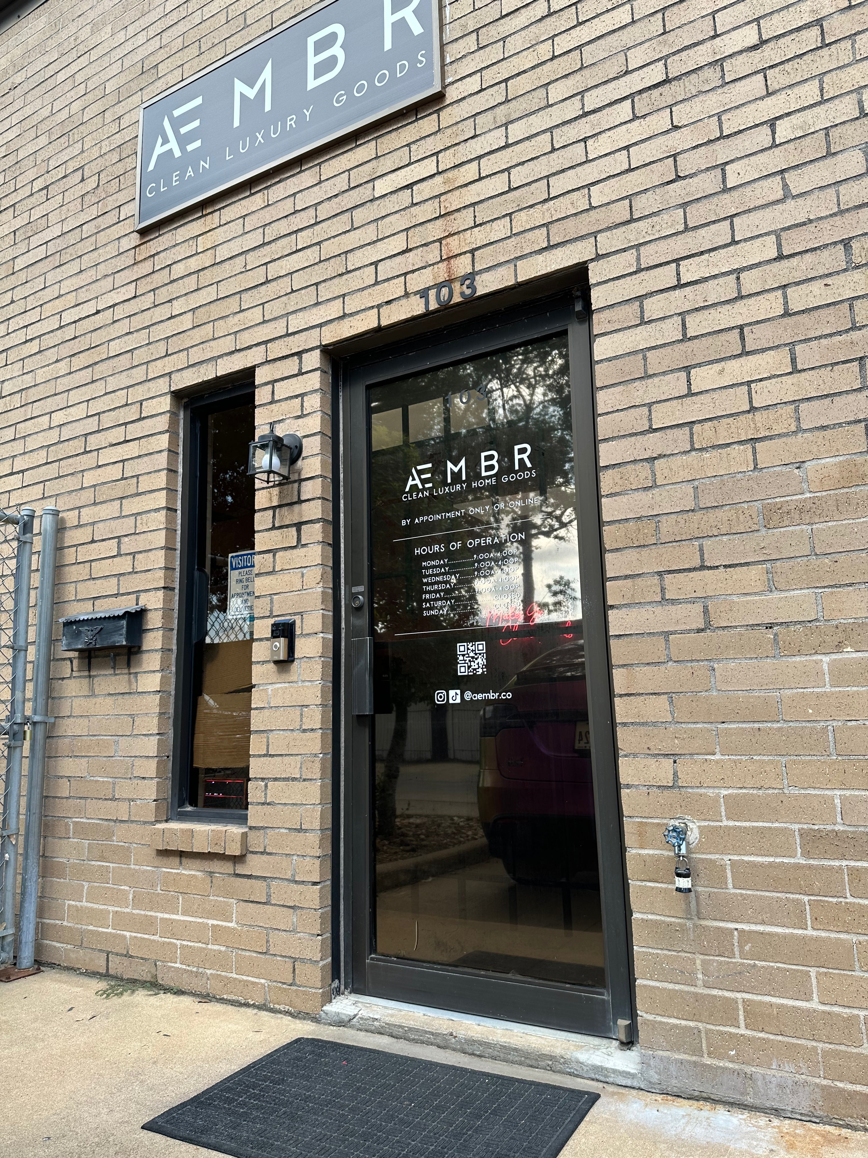 AEMBR store entrance with glass door, branded sign, and clean brick exterior.