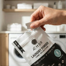 Hand opening AEMBR Laundry Powder trial pack in a modern laundry room, non-toxic detergent.