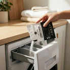 Hand pouring AEMBR laundry powder into washing machine drawer in a modern laundry room