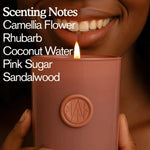 Woman smiling, holding a lit AEMBR non-toxic candle with scent notes listed on the image.