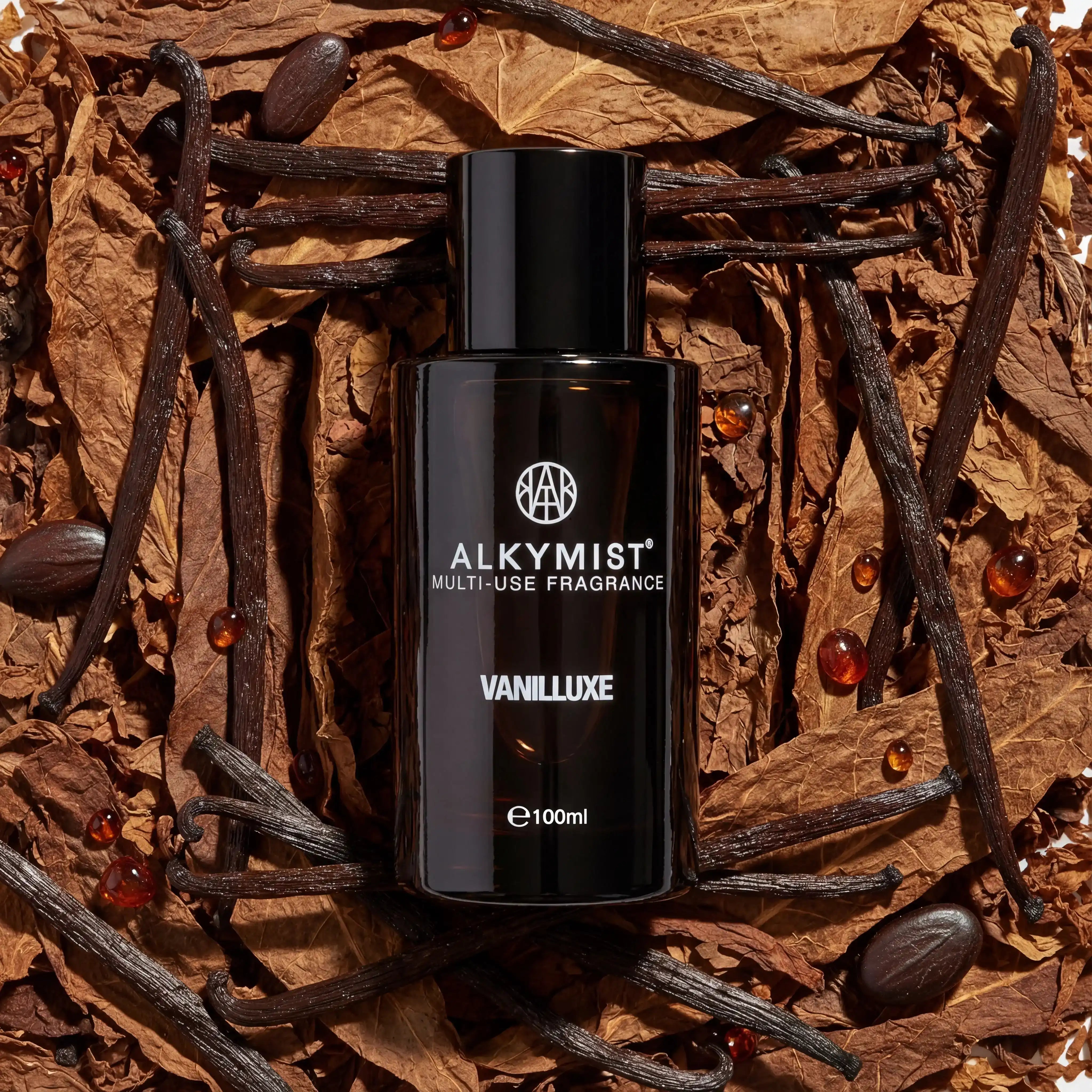 AEMBR ALKYMIST Vanilluxe fragrance bottle on dried leaves, vanilla beans, and amber beads