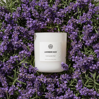White candle labeled 'Lavender Haze' surrounded by purple lavender flowers