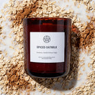 AEMBR Spiced Oatmilk candle in amber glass, surrounded by oats, cinnamon, and oat milk.