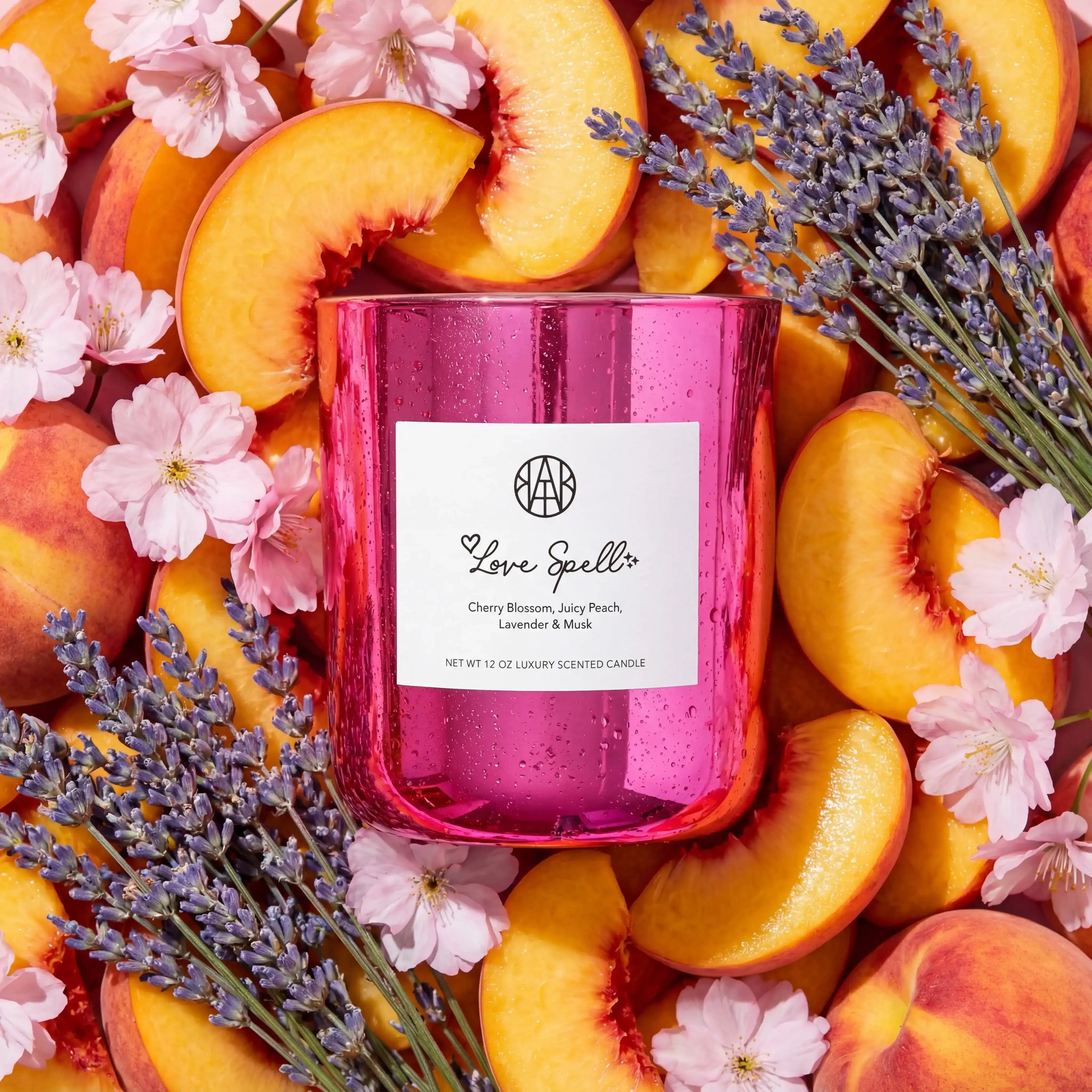 AEMBR Love Spell scented candle in pink glass, surrounded by peach slices, cherry blossoms, and lavender