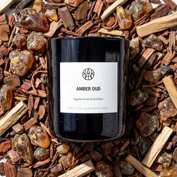 AEMBR Amber Oud Candle with warm amber-colored wax and elegant glass holder, perfect for creating a cozy ambiance.