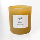 A lemon-scented Citron Candle by AEMBR with a simple glass holder and a lit wick, emitting a warm, inviting glow.