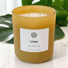 AEMBR citron candle in a glass jar with a lit wick, showcasing its fresh citrus scent and bright yellow color.