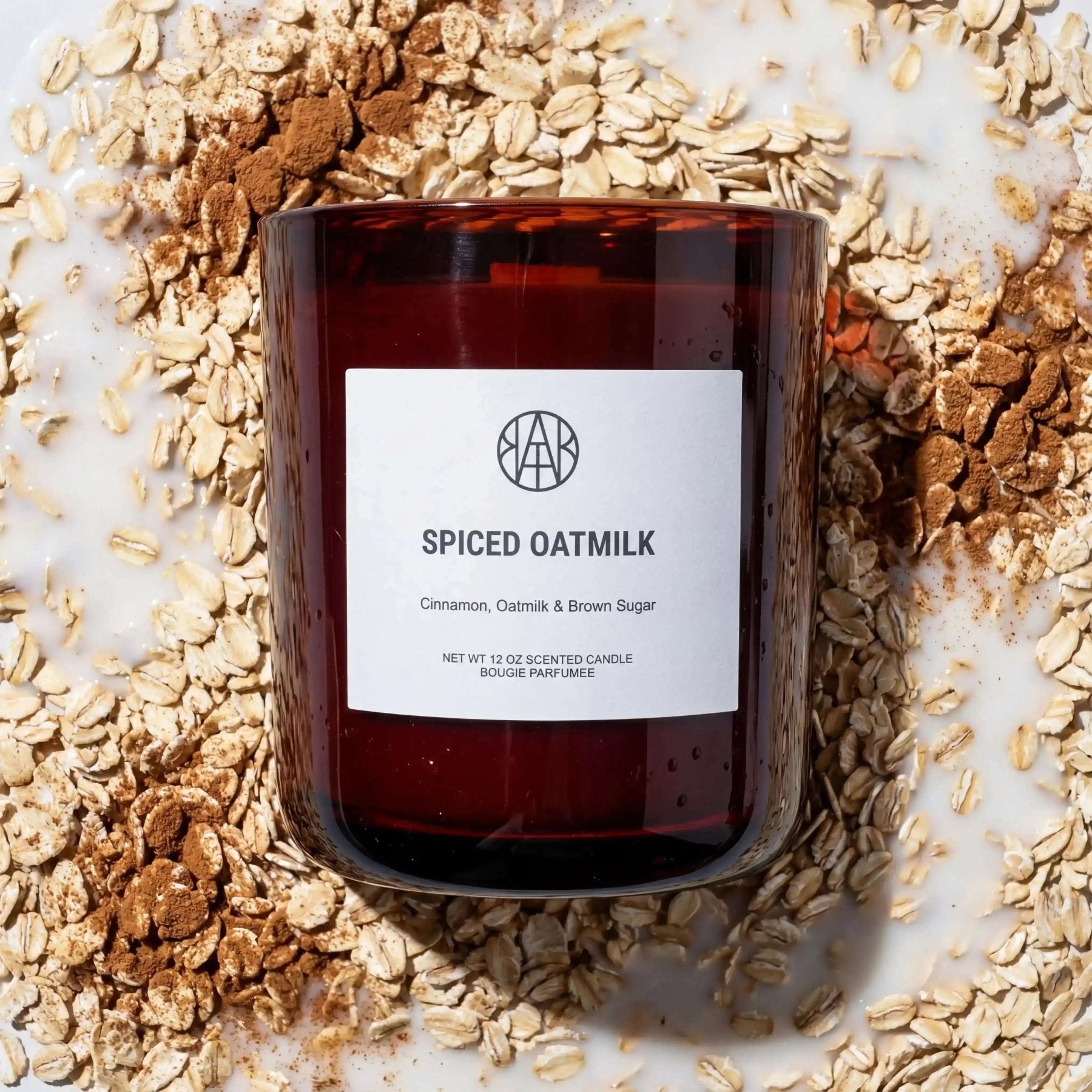AEMBR Spiced Oatmilk Candle with a sleek glass jar, featuring a warm, inviting scent and a soft flickering flame.