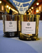 Non-toxic scented candles Juletid and Fraser Fir in gold jars on a festive outdoor table