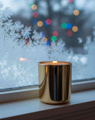Non-toxic candle in gold container on winter windowsill with frosted glass and bokeh lights
