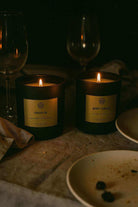 Two lit non-toxic candles on a dinner table, labeled Fraser Fir and Berry + Embers, moody ambiance