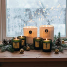 Non-toxic winter candles with pinecones and greenery on a wooden table by a frosted window