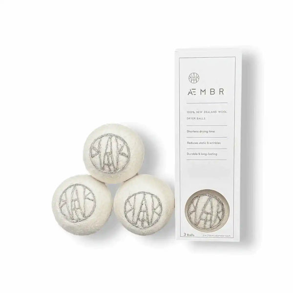 Set of AEMBR wool dryer balls in natural colors, shown with laundry essentials including detergent, linen spray, and oxygen boost.