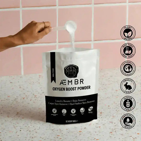 AEMBR Oxygen Boost laundry additive in a clear container with a scoop, part of the Fjord laundry bundle including dryer balls and linen spray.