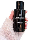 AEMBR ALKYMIST® Luxe Amber Oud multi-use fragrance bottle with elegant design and amber-colored liquid.