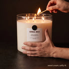 In use — hands lighting the large Cereal Milk Valkyrie candle with a match, warm amber glow