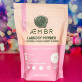 Package of AEMBR laundry powder with a colorful bokeh background