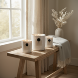 Three white candles with black dots on a wooden table near a window with light curtains.