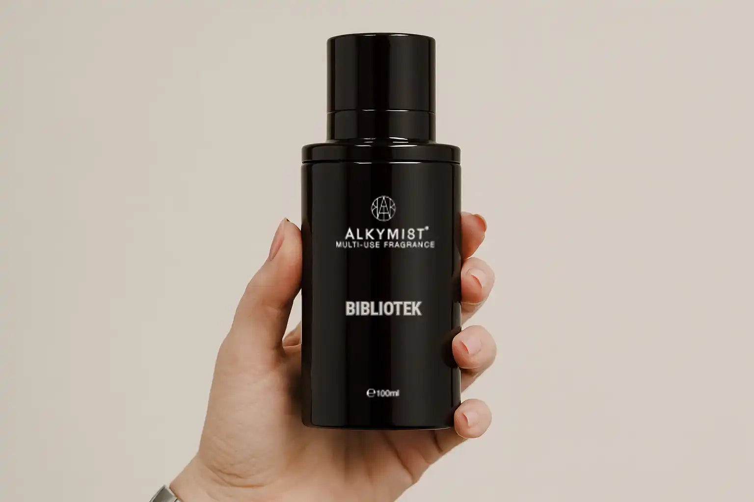 Hand holding AEMBR ALKYMIST multi-use fragrance bottle labeled BIBLIOTEK, minimalist background