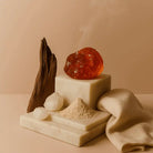 AEMBR amber oud stone, driftwood, and natural powder on marble blocks with a beige cloth