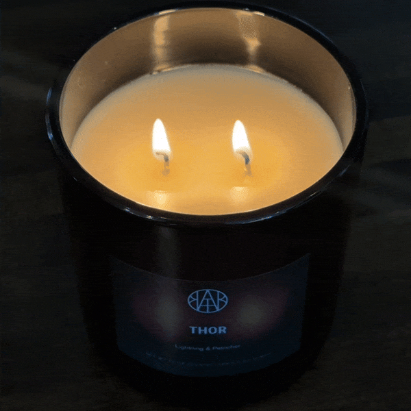 Non-toxic double wick candle in black glass jar, Thor scent, burning on wood surface