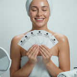 Woman holding skincare products with a towel on her head in a bathroom setting