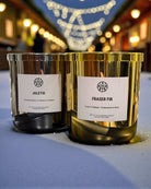 AEMBR Juletid and Fraser Fir non-toxic candles in gold jars on a festive outdoor table with string lights