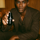 Man in brown suit holding AEMBR non-toxic product bottle, seated in modern wood interior