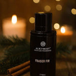 Black fragrance bottle labeled 'Fraser Fir' by Alkymist on a wooden surface with candles and cinnamon sticks in the background.