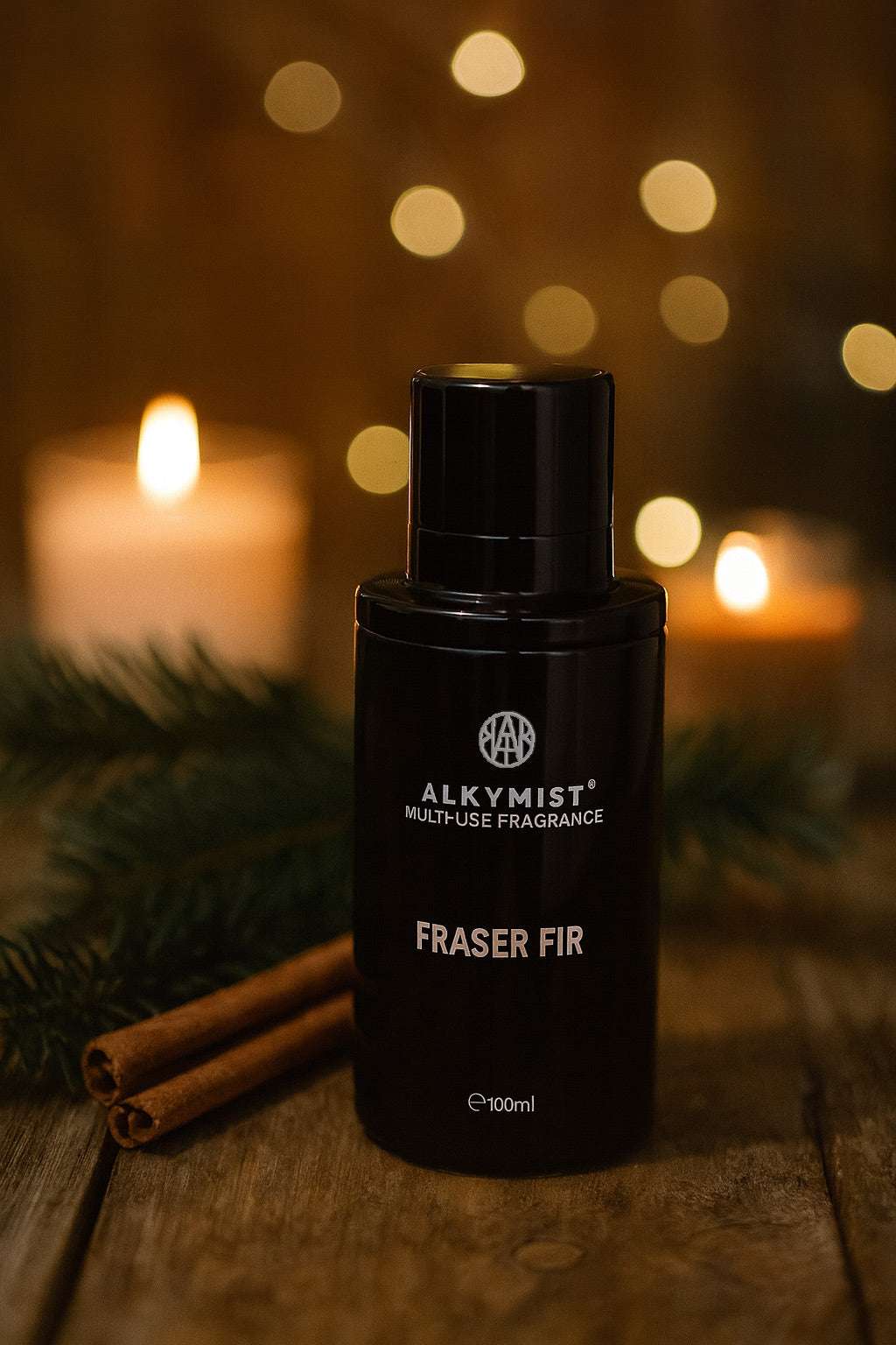 Black fragrance bottle labeled 'Fraser Fir' by Alkymist on a wooden surface with candles and cinnamon sticks in the background.