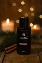 AEMBR Alkymist Fraser Fir fragrance bottle on wood with pine, cinnamon sticks, and candlelight.
