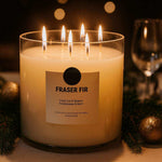 AEMBR Fraser Fir non-toxic candle burning on elegant holiday dinner table with fir branches and gold ornaments.