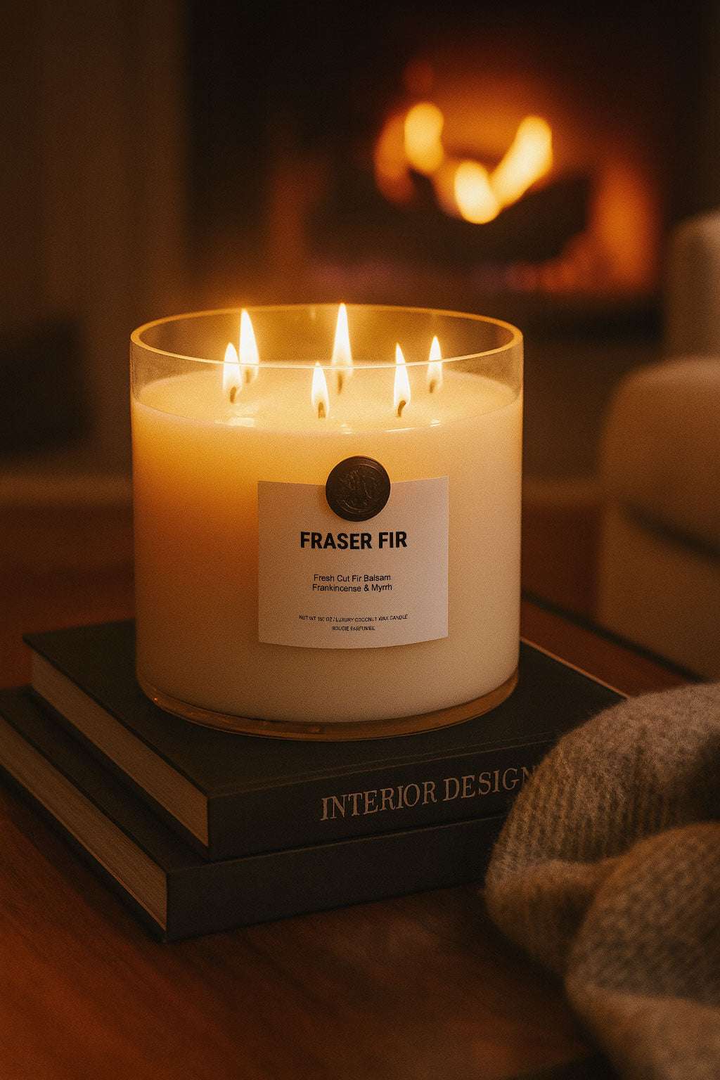 Candle labeled 'Fraser Fir' on a stack of books with a fireplace in the background