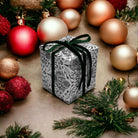 AEMBR holiday gift box with floral wrapping and black ribbon, surrounded by ornaments and pine.